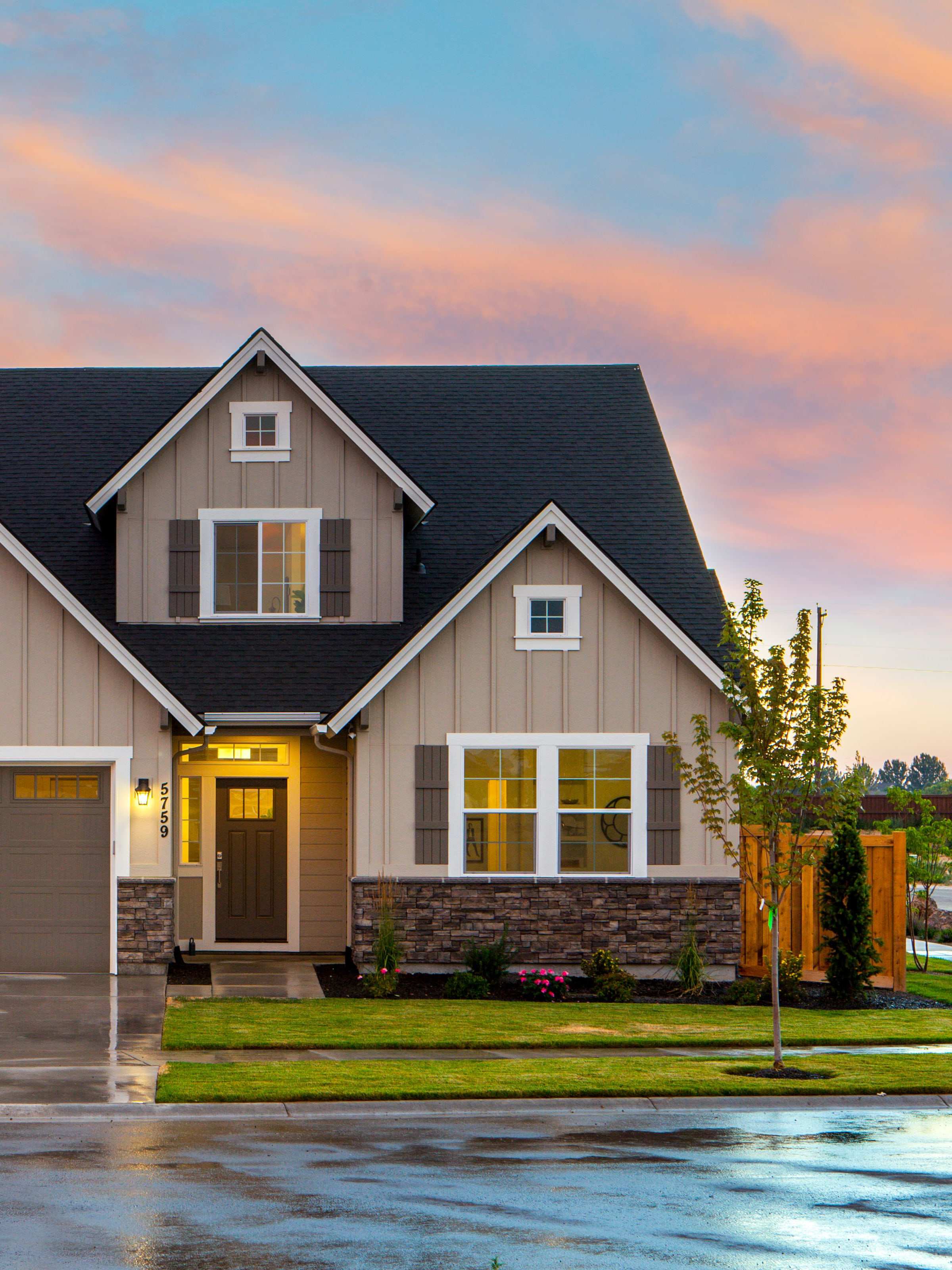 Dusk view of a Texas farmhouse plan with gables, warm interior light, and a stone wainscot