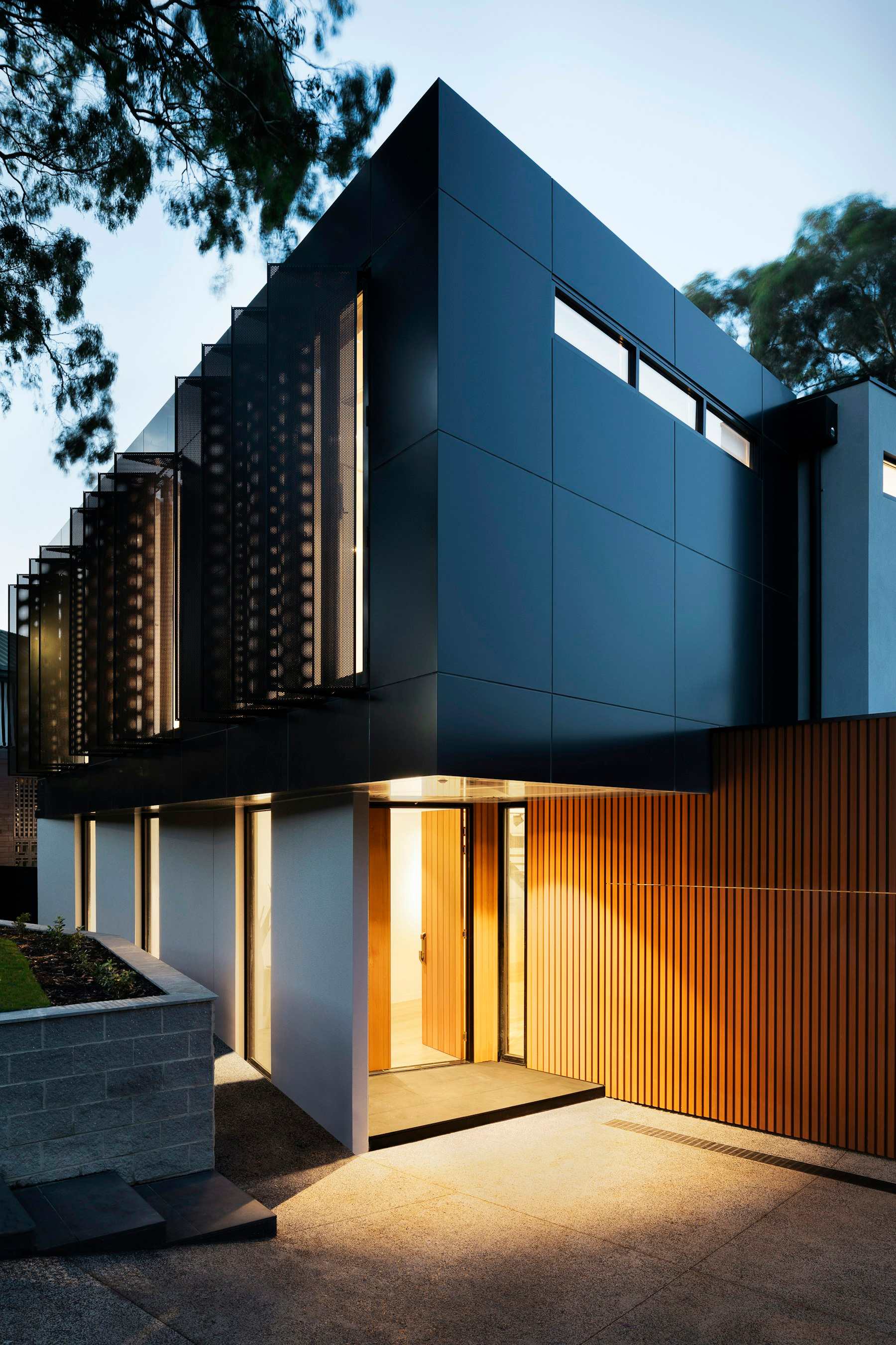 Twilight view of a contemporary custom home with black cladding, warm wood, and glowing interior light